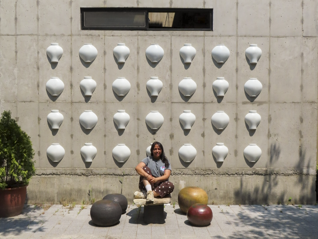 Piya seated in front of a concrete wall of white ceramic vessels